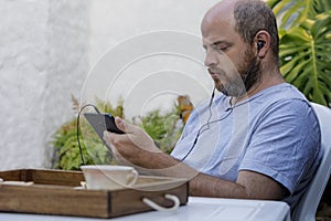 In an outdoor garden a man is looking intently at a digital tablet with headphones for listening