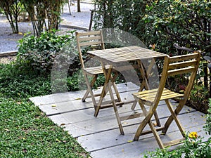 Outdoor garden table set. Empty wooden table and two chairs on concrete floor on green grass.