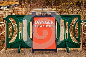 Outdoor green modular gate on public pebble and concrete sidewalk with sandwich sign reading DANGER Area Closed - Woods and