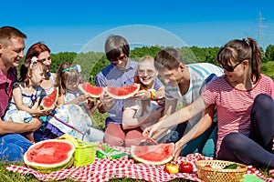 Outdoor group portrait of happy company having picnic on green grass in park and enjoying watermelon