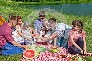 Outdoor group portrait of happy family having picnic near the lake and enjoying watermelon