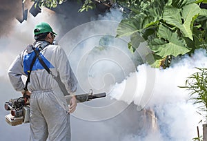 Outdoor healthcare worker using fogging machine spraying chemical to eliminate mosquitoes on overgrown at slum area