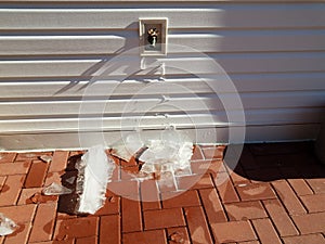 Outdoor hose spigot with ice and red bricks in winter
