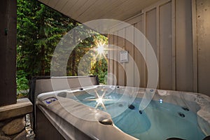 A outdoor hot tub near a forest with a sunburst coming through the trees.