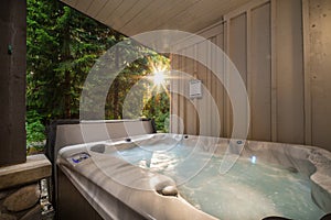 A outdoor hot tub near a forest with a sunburst coming through the trees.