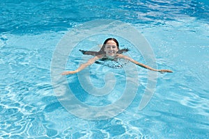 Outdoor image of cheerful adorable young lady enjoying active pasttime, fond of leisure activities, swimming in swimming pool