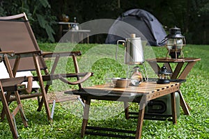 Outdoor kettle, portable gas stove, bowl and vintage lanterns with outdoors table set on green lawn in camping area