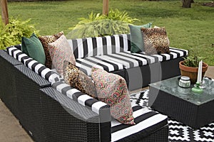 Outdoor lawn furniture with black and white crisply striped upholstery and assorted pillows grouped around a table with ferns on a