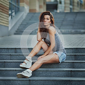 Outdoor lifestyle portrait of pretty young girl posing on stairway, wearing in hipster urban style on urban background