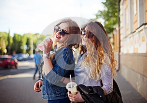 Outdoor lifestyle portrait of two happy best friend girls walk laugh talk and drink lemonade. Girls laugh at the joke