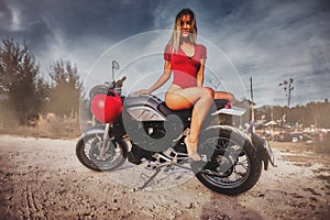 Outdoor lifestyle portrait of young sexy woman in red swimsuit sitting on a vintage custom motorcycle