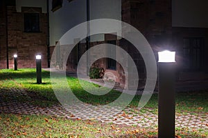 Outdoor lights in front of an old building illuminating a walkway in the garden at night