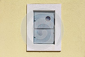 Outdoor locked metal electrical meter box with switch box mounted on house wall with new facade surrounded with white frame