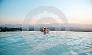 Outdoor luxury resort. Woman relaxing in nature swimming pool water. Sunset in the edge pool with beautiful view. Happy