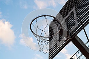 Outdoor metalic street basketball hoop with a blue sky in background.