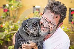 Outdoor nice portrait of adult caucasian man with black beard and same color old funny dog pug - garden in background and best
