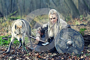 Outdoor northern warrior woman with braided hair and war makeup holding shield and ax with wolf next to her ready to attack -