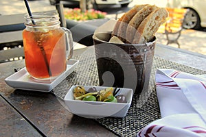 Outdoor patio table at restaurant, with iced tea,stuffed olives and fresh bread on placemat
