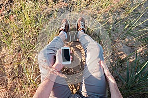 Outdoor photo of man sitting on grass holding phone with blank screen.