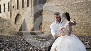 Outdoor photosession of loving stylish bride and groom on stony shore near the castle. Action. Beautiful wedding couple