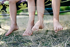 Outdoor picture of two children legs barefoot. Closeup of happy kids sitting on sunny countryside.
