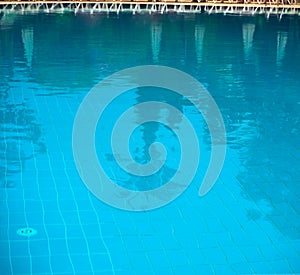 Outdoor pool. Palm trees and sun umbrellas are reflected in the water.