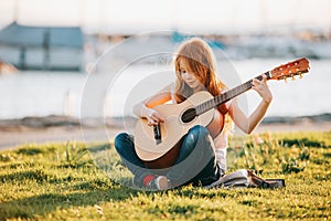 Outdoor portrait of adorable 9 year old kid girl playing guitar outdoors