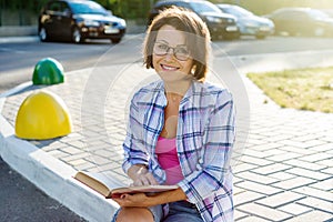 Outdoor portrait of an adult beautiful woman reading a book whil