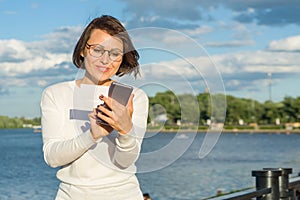 Outdoor portrait attractive happy middle aged woman female freelancer blogger traveler with phone on nature