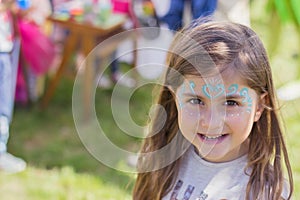 Outdoor portrait of a beautiful little girl with painted face