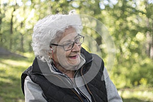 Outdoor portrait of beautiful senior woman with curly white hair. Elderly lady in park