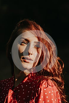 Outdoor portrait of a beautiful young adult woman with full lips green eyes red hair and dressed in red country road shirt with
