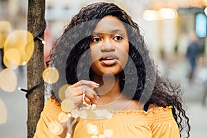 Outdoor portrait of a beautiful young african plus size woman student with cute smile, holds garland with warm light in