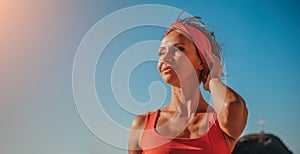 Outdoor portrait of beautiful young brunette woman in red sport suit with red headband on the beach at sunrise near the