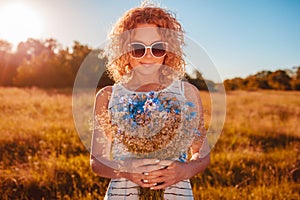 Outdoor portrait of beautiful young woman with red curly hair holding bouquet of flowers. Allergy free