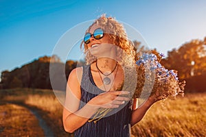 Outdoor portrait of beautiful young woman with red curly hair holding flowers. Summer mood.