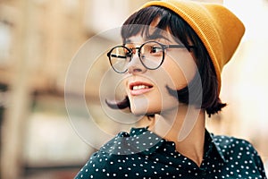 Outdoor portrait of beautiful young woman wearing green shirt with white dots and transparent eyeglasses, smiling and laughing.