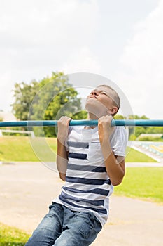 Outdoor portrait of blond boy teenager, young man on brachiating bar at a school yard. Boy doing pull ups.