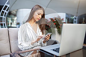 Outdoor portrait of caucasian businesswoman using wireless Internet connection on laptop and gadgets, messaging via popular social