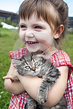 Outdoor portrait of a cute little girl with small kitten, girl playing with cat on natural background