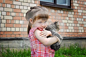 Outdoor portrait of a cute little girl with small kitten, girl playing with cat on natural background