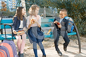 Outdoor portrait of elementary school students with lunch boxes, healthy school breakfast. Children eat, talk, laugh