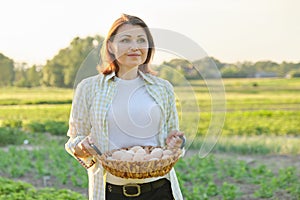 Outdoor portrait of farmer woman with basket of fresh chicken eggs, farm