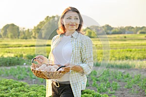 Outdoor portrait of farmer woman with basket of fresh chicken eggs, farm