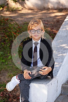 Outdoor portrait of Fashionable Schoolboy with glasses, school uniform, blonde boy with long hair