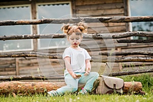 Outdoor portrait of a girl sitting on the grass near the fence.Summer in the village. beautiful baby girl on a wooden bench.