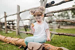 Outdoor portrait of a girl sitting on the grass near the fence.Summer in the village. beautiful baby girl on a wooden bench.