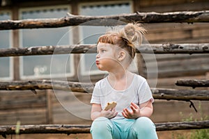 Outdoor portrait of a girl sitting on the grass near the fence.Summer in the village. beautiful baby girl on a wooden bench.