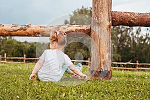 Outdoor portrait of a girl sitting on the grass near the fence.Summer in the village. beautiful baby girl on a wooden bench.