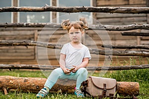 outdoor portrait of a girl sitting on the grass near the fence.Summer in the village. beautiful baby girl on a wooden